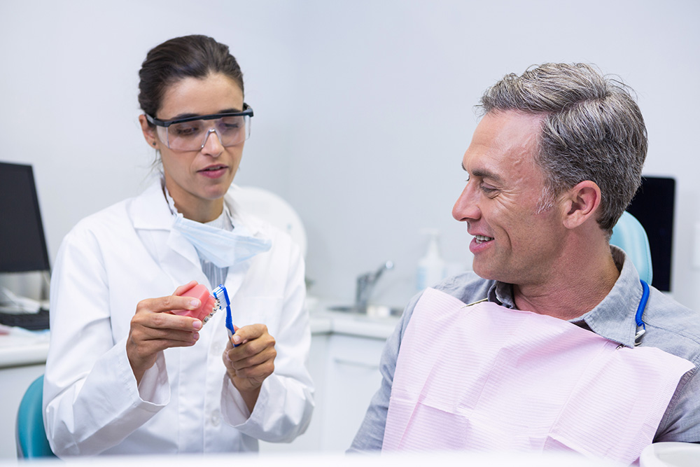 dentist teaching man brushing teeth on dental mold